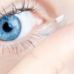 Closeup of a blue eye and a finger putting a contact lens in