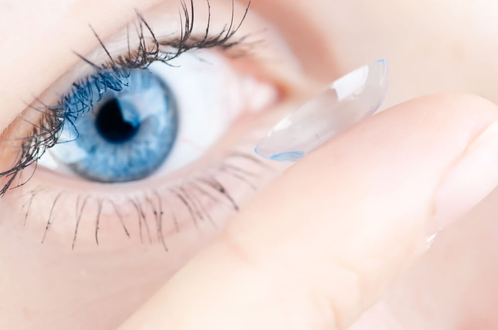 Closeup of a blue eye and a finger putting a contact lens in